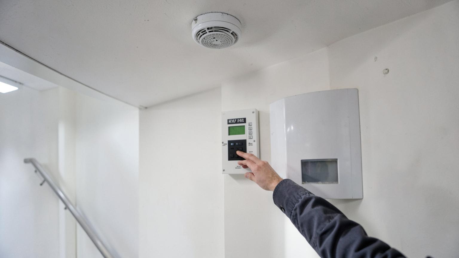 Smoke detector and fire alarm panel being checked in a communal stairwell